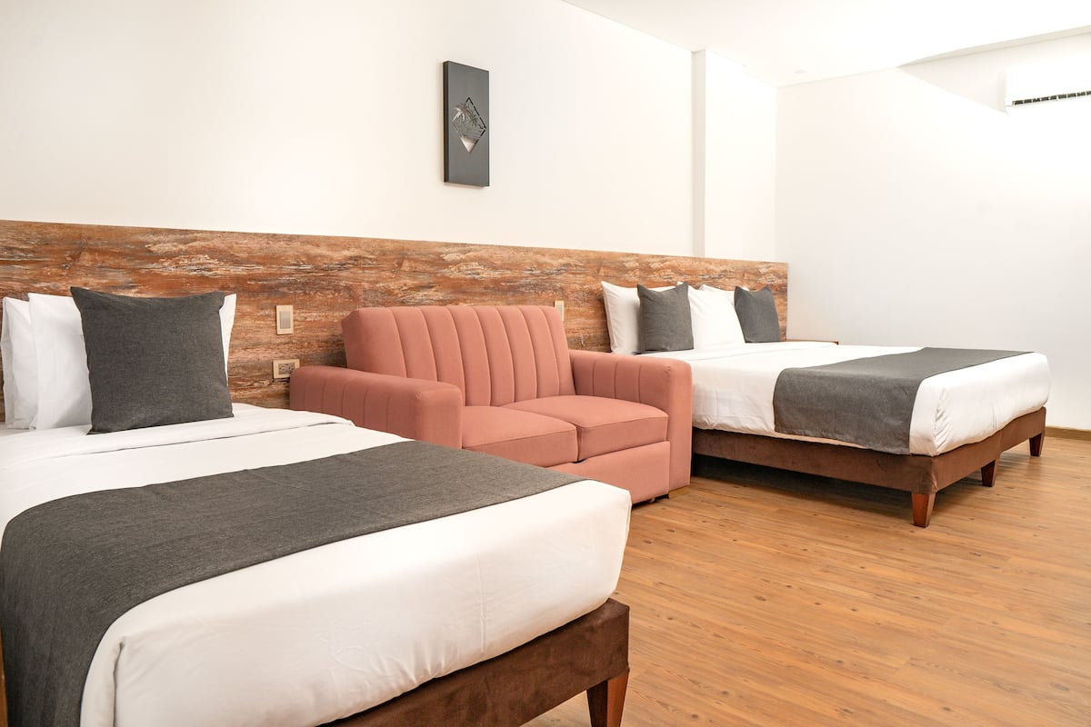 Habitación de hotel con dos camas, cabecero de madera y una pequeña zona de estar.
