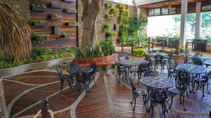 Een terras buiten met houten vloer, metalen tafels en stoelen, en diverse planten en groen.