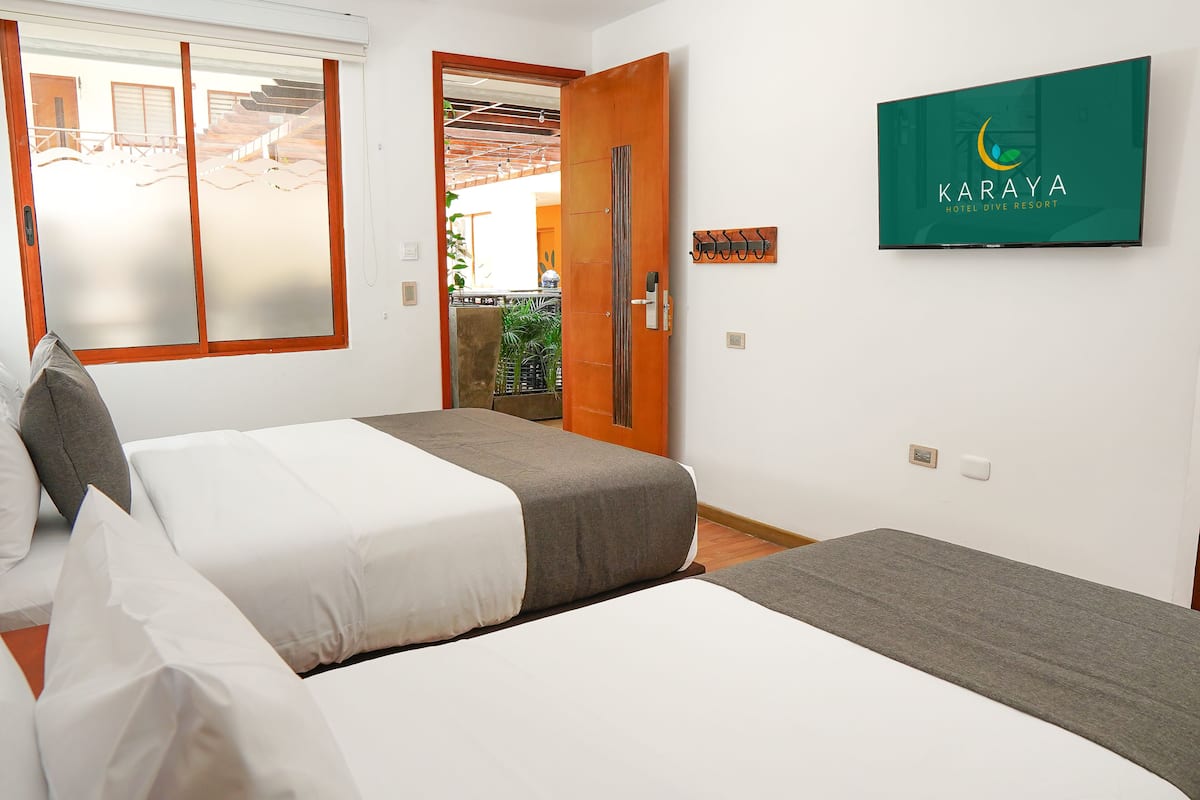 Habitación de hotel con dos camas, puerta corrediza a un balcón y un televisor montado en la pared mostrando el nombre del hotel.