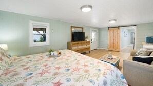 A bedroom with a bed, dresser, TV, and a sliding door. - Salt and Sand Studio (Downstairs Only) (Panama City Beach)