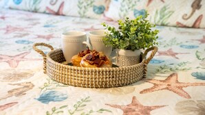 A woven basket containing two mugs and a small potted plant on a bed with a starfish-patterned bedspread. - Salt and Sand Studio (Downstairs Only) (Panama City Beach)