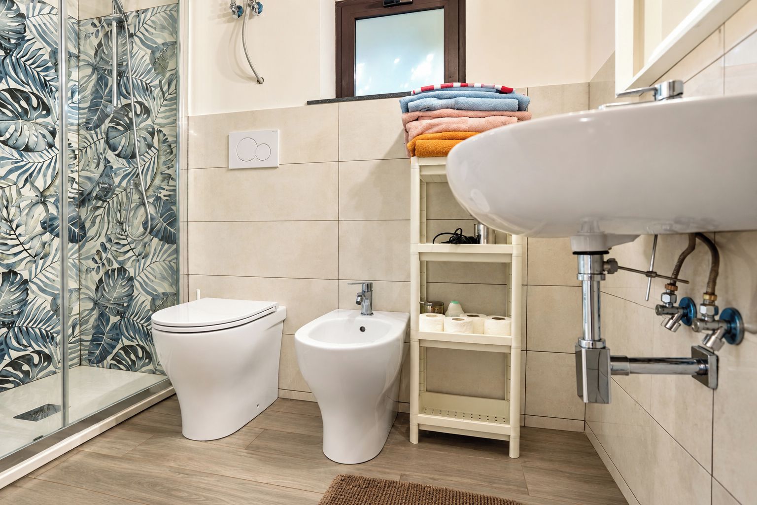 A bathroom with a toilet, bidet, and sink, with a shower area and a towel rack.