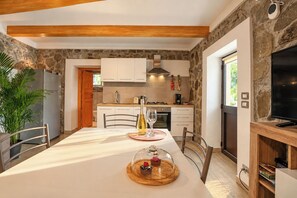 Una cocina moderna con pared de piedra, vigas de madera en el techo y un comedor con una mesa dispuesta para dos.