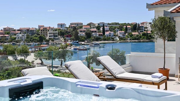 A rooftop terrace with a hot tub, lounge chairs, and a view of a marina and buildings.