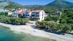 A coastal hotel with multiple buildings, a sandy beach, and a mountainous backdrop.