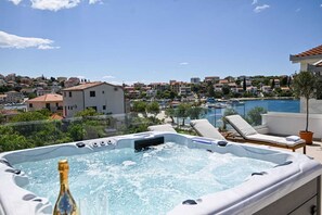 A hot tub with a champagne bottle, lounge chairs, and a view of a residential area and a pool. - Luxury apartment literally on the beach - whirlpool and sauna (Seget Vranjica)