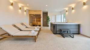 A spa room with three sunbeds, a sauna, and a hot tub.