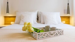A neatly made bed with white linens, a tray with flowers and cups, and pendant lights above.