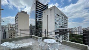 Terraza en la azotea con zona de estar, que incluye una mesa y sillas, con vistas a un paisaje urbano de edificios modernos.