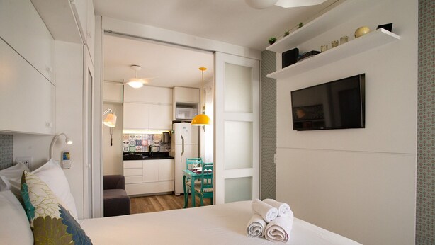 Una habitación de hotel con una cama, televisor, escritorio y kitchenette.