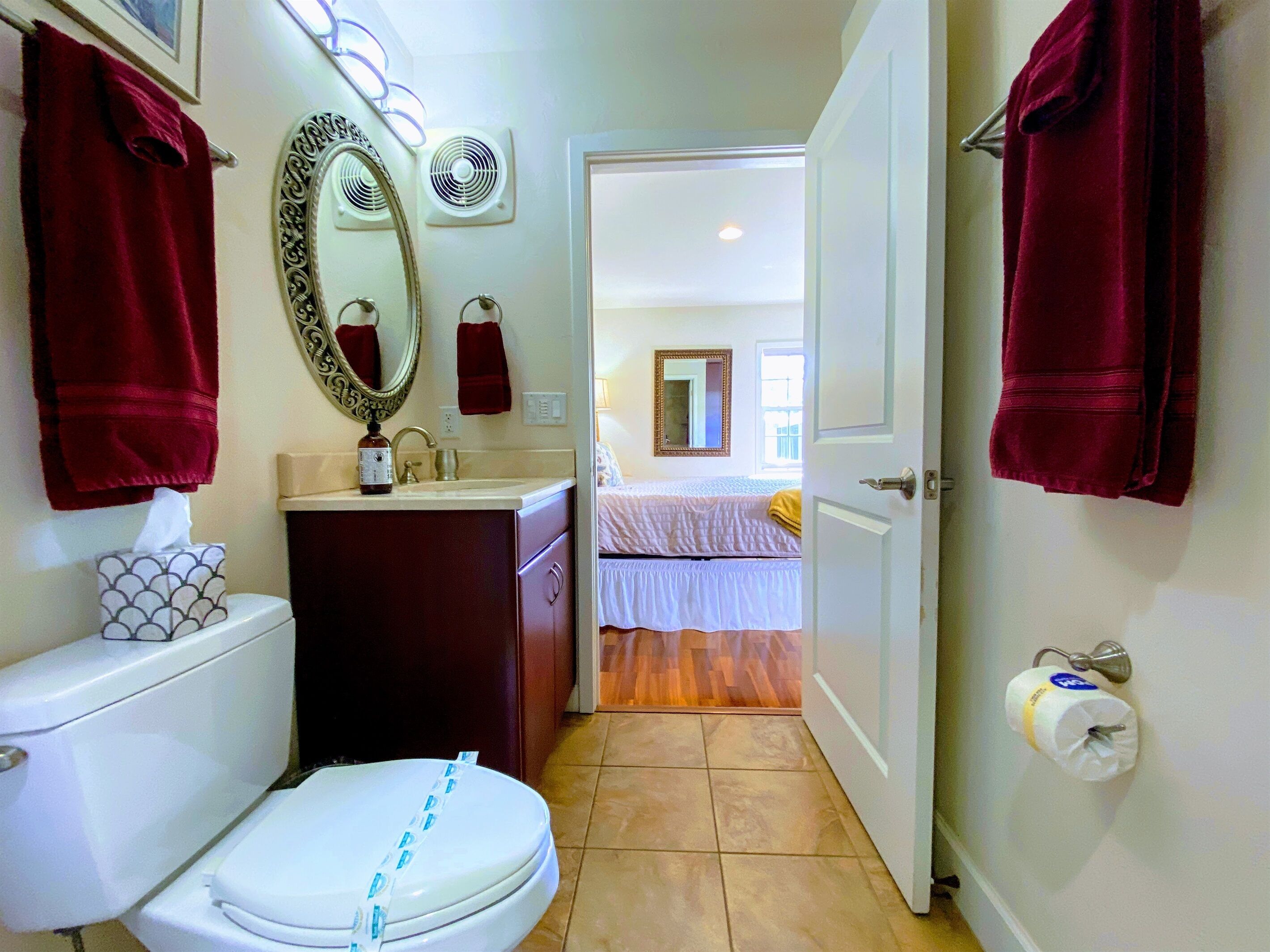 Un bagno con il water, lavandino e specchio. Asciugamani appesi al muro e porta carta igienica.