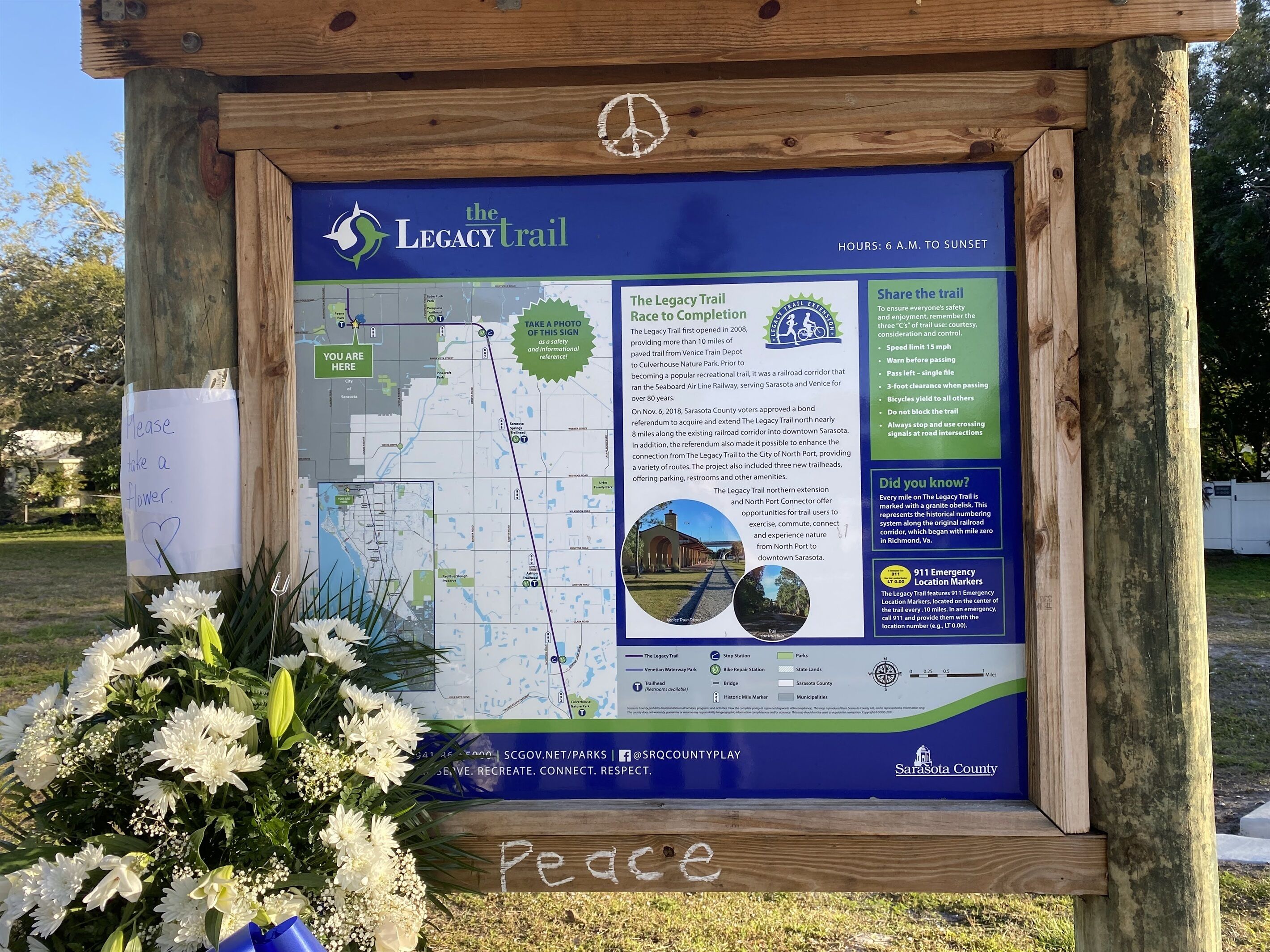 A wooden signboard with a map and information about The Legacy Trail, including its hours of operation and safety guidelines.