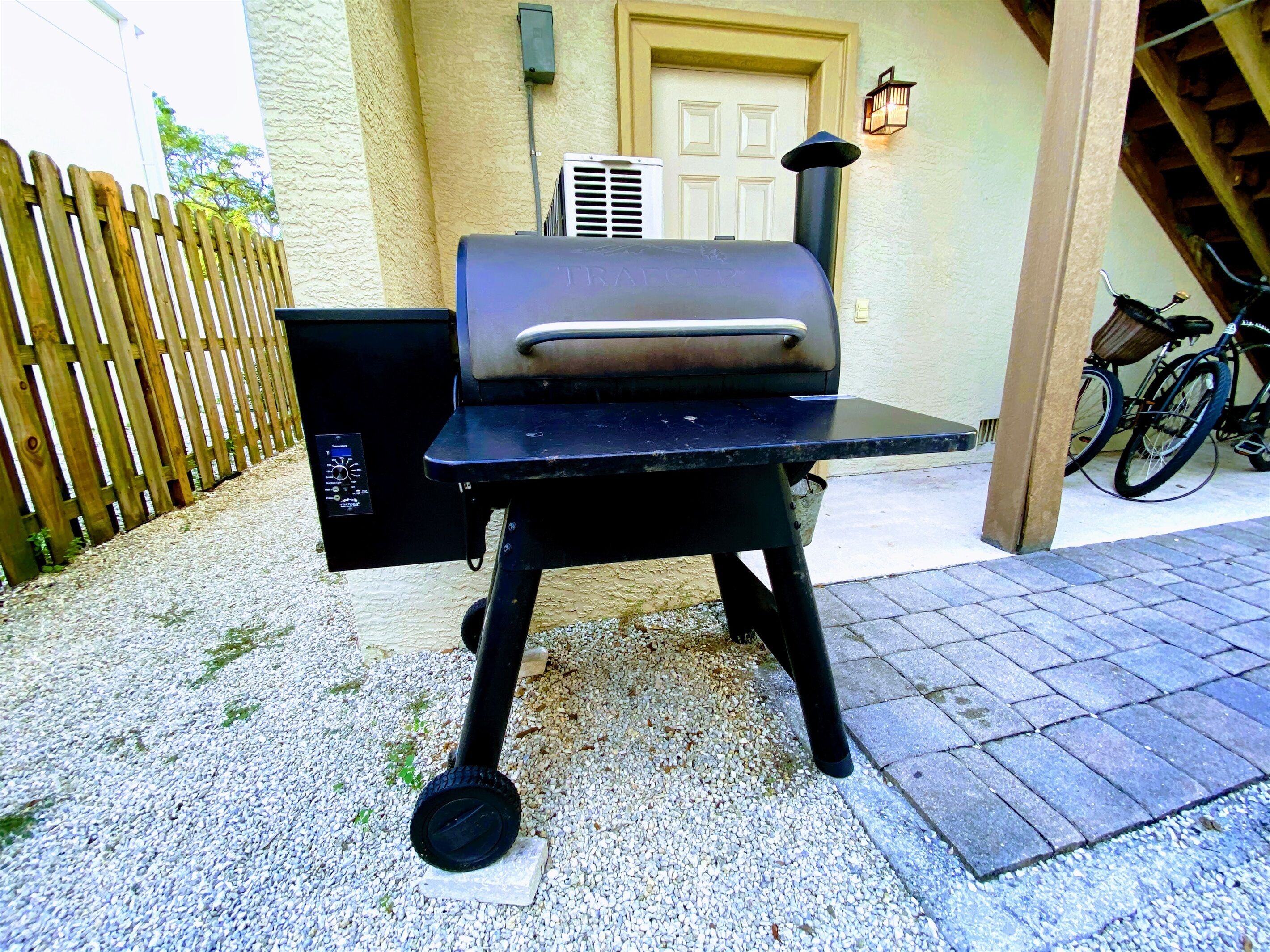 Un barbecue doté d’un écran numérique, placé sur une surface de gravier devant une clôture en bois et un bâtiment muni d’une porte et d’un luminaire fixé au mur.