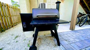 Un barbecue doté d’un écran numérique, placé sur une surface de gravier devant une clôture en bois et un bâtiment muni d’une porte et d’un luminaire fixé au mur.