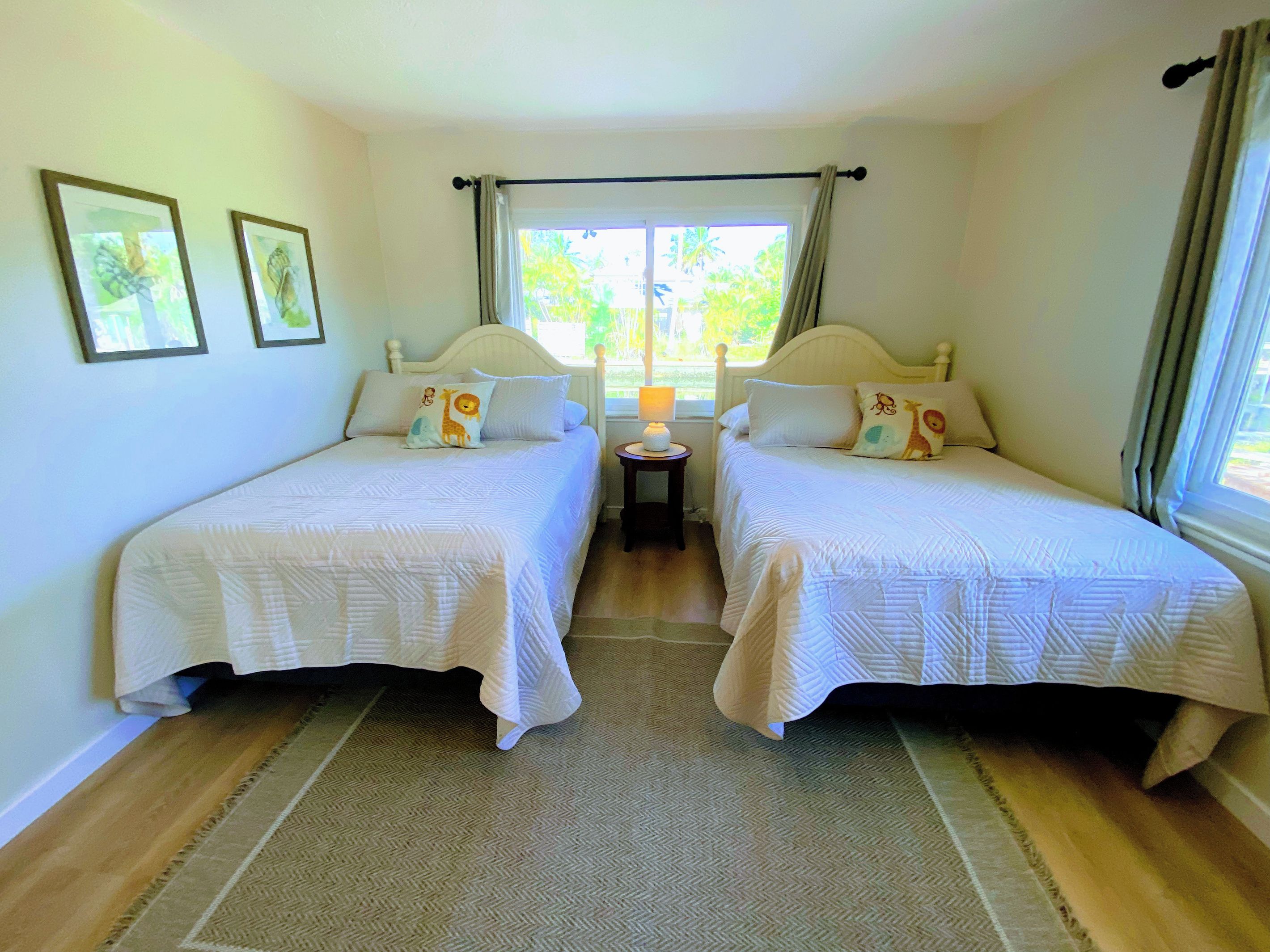 A double room with two beds, a small bedside table with a lamp, and a window with curtains.