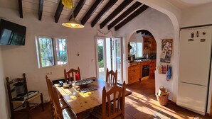 Una cucina con mobili in legno, un frigorifero, un tavolo da pranzo con sedie e un televisore montato a parete.