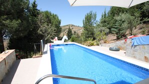 Una piscina con un galleggiante a forma di unicorno bianco, circondata da alberi e un muro in pietra.