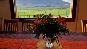 Un tavolo con un vaso di fiori e vista su un campo verde e montagne attraverso una finestra.