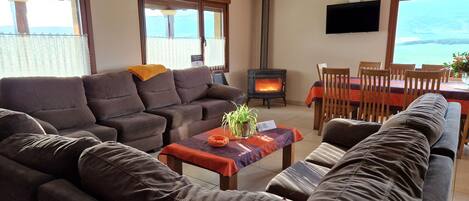 A living room with a sofa set, a table with a plant, a fireplace, and a dining area with chairs.