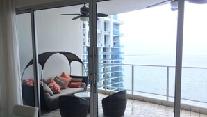 A balcony with a glass door, a sofa with cushions, a chair, and a ceiling fan.