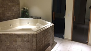 A bathroom with a large bathtub, a tiled shower area, and a door leading to another room.