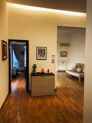 Uma sala de estar moderna com piso de madeira, um sofá, uma mesinha com objetos decorativos e uma porta de entrada para outro cômodo.