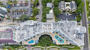 Luchtbeeld van een hotel met meerdere parkeerplaatsen, een centraal gelegen zwembad en omliggend groen.