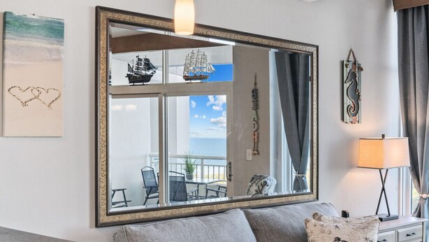Een woonkamer met een grote spiegel die een balkon weerkaatst, met stoelen en een modelboot.