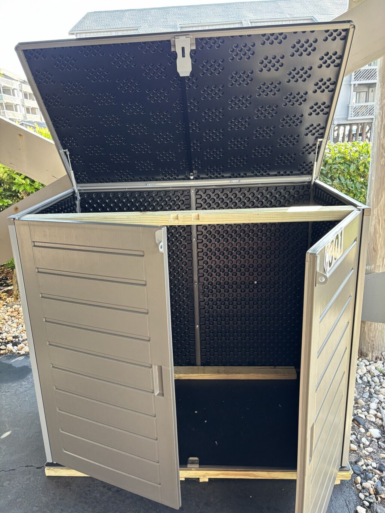 Un meuble de rangement en métal doté d’une porte à charnières, d’un toit en métal texturé et d’une base en bois.