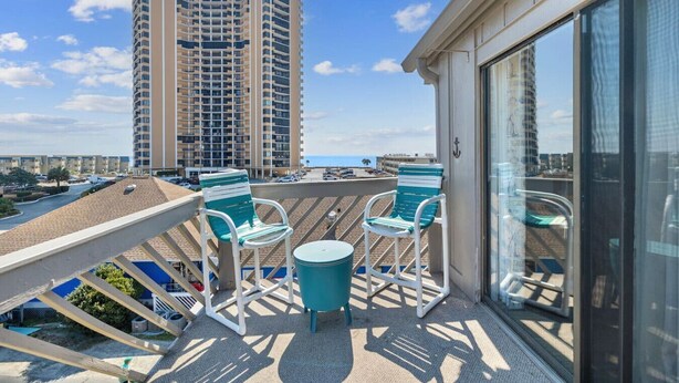 A balcony with two chairs and a small table, overlooking a cityscape and a body of water. - 3rd Floor Ocean View, Pools/Hot Tub- Shore Dr (Myrtle Beach)