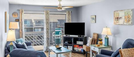 A living room with a TV, sofa, and coffee table. There is a balcony with a view.