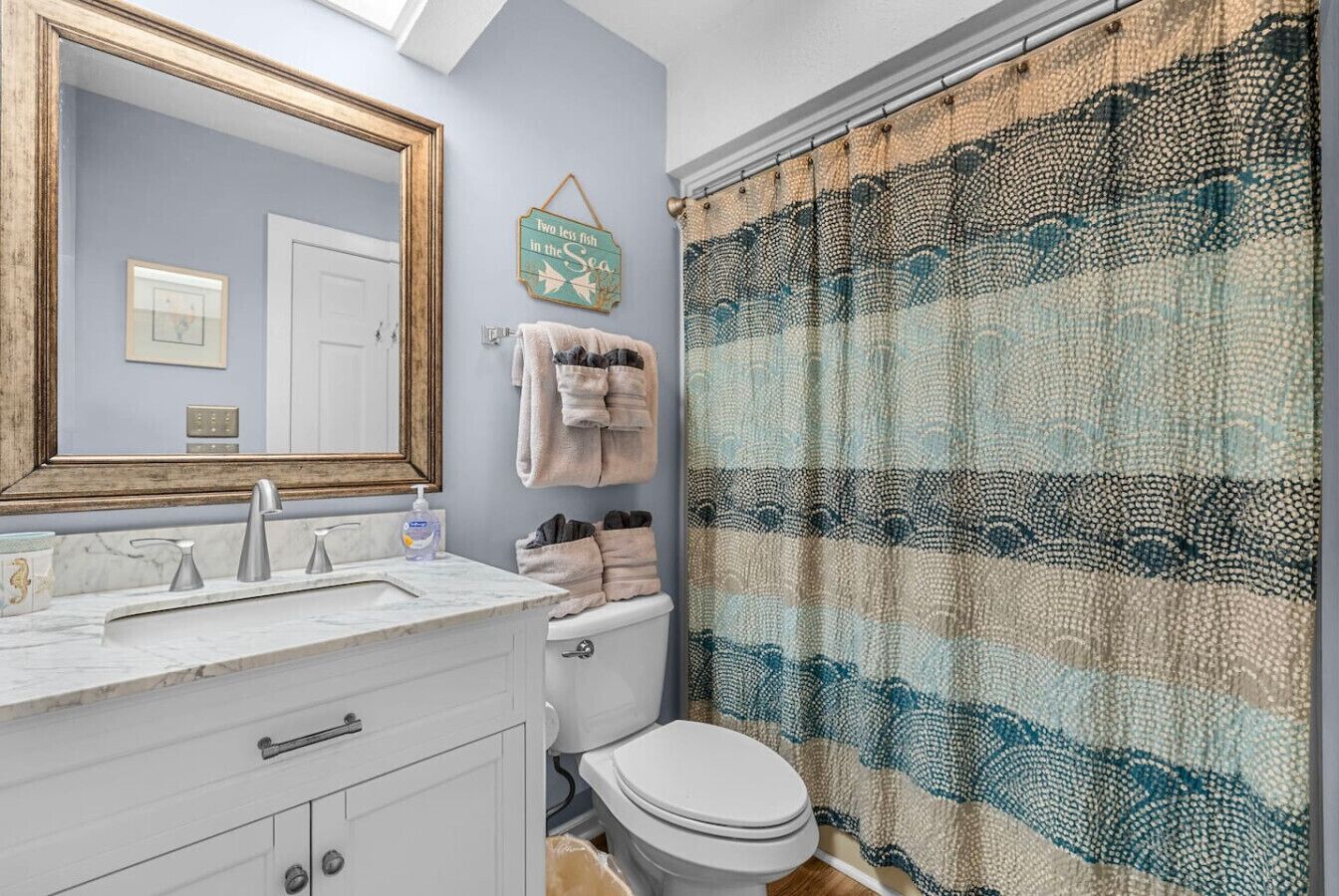 A bathroom with a white sink, mirror, and toilet. There is a towel rack with towels and a decorative sign on the wall.
