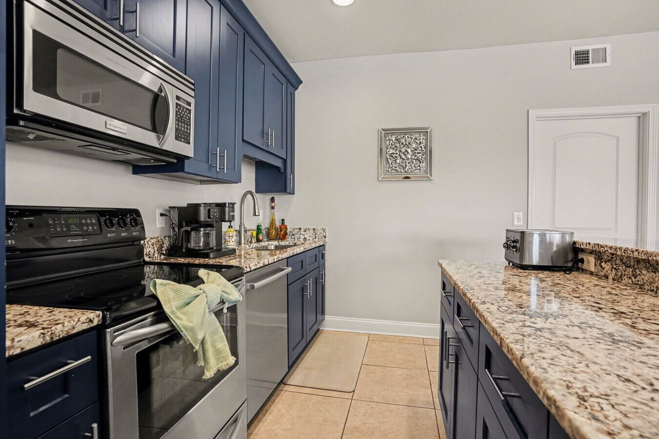 A kitchen with dark blue cabinets, a stainless steel stove, a microwave, a coffee maker, and a toaster.