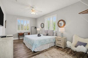 A bedroom with a bed, bedside tables, a chair, a ceiling fan, and windows.