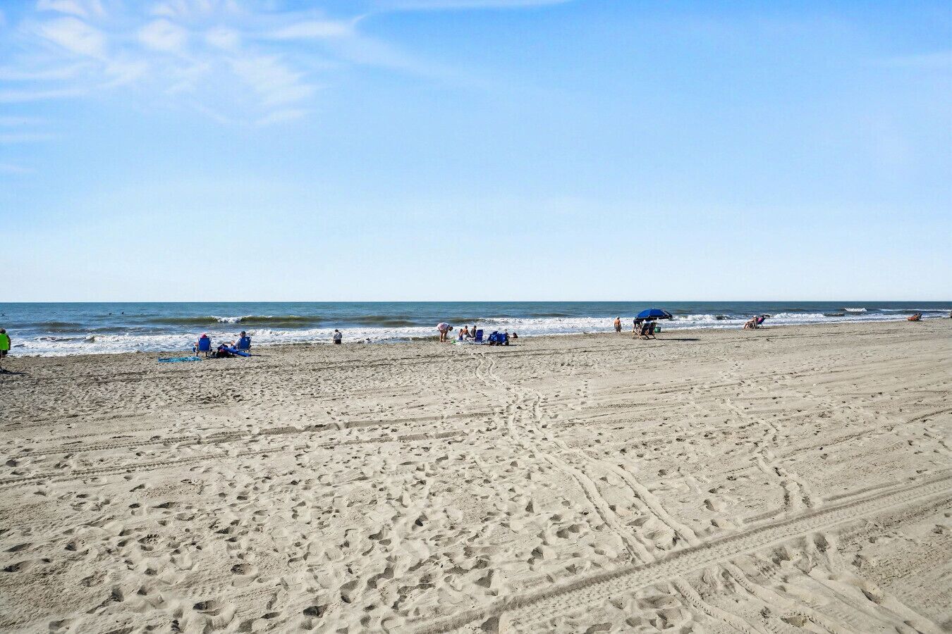 Ein weiter Sandstrand mit Fußabdrücken, einigen Badegästen und einem klaren Himmel.