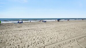 Una extensa playa de arena con huellas, algunas personas y un cielo despejado.