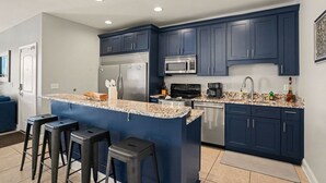 Una cocina moderna con armarios azul oscuro, electrodomésticos de acero inoxidable, encimera de granito y taburetes de bar.