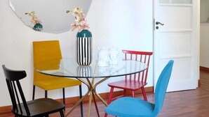 Un comedor con una mesa de vidrio, cuatro sillas, un espejo grande y un jarrón con flores.