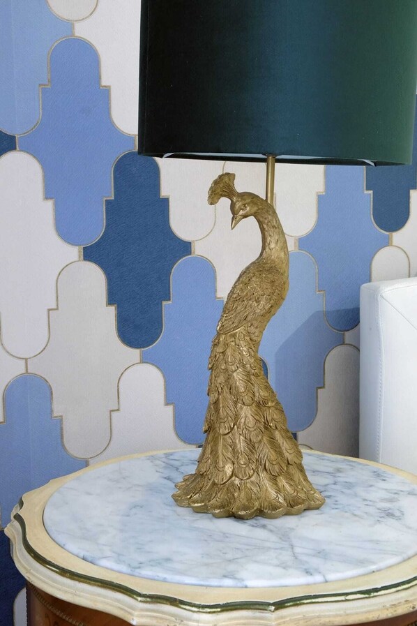 Una estatua dorada de un pavo real sobre una mesa de mármol, frente a una pared con diseño.