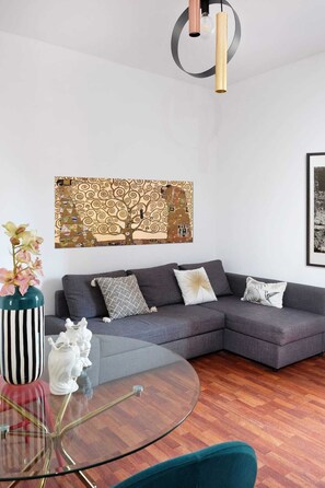 Una sala moderna con un sofá seccional gris, una mesa de centro de vidrio y un adorno de pared decorativo.