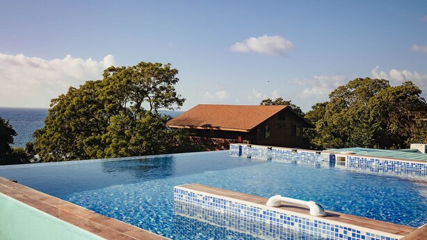A swimming pool with a view of the ocean and a wooden building in the background. - Cozy 1 Bedroom Suite with Easy Beach Access (West Bay)