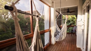 Une terrasse en bois avec deux hamacs, une chaise et une vue sur la verdure, grâce à de grandes fenêtres.