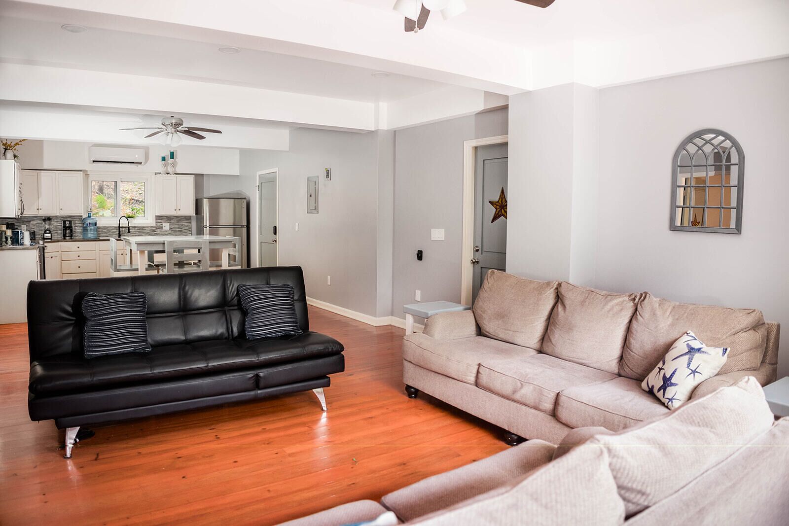 Ein modernes Wohnzimmer mit einer schwarzen Ledersofa, einem hellen Sofa, Holzböden und einem Deckenventilator.