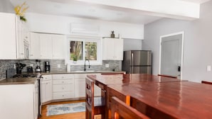 A modern kitchen with white cabinets, a stainless steel refrigerator, and a wooden dining table.
