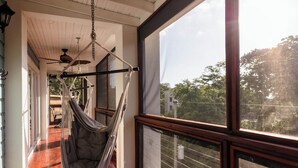 Una habitación con una silla hamaca, ventilador de techo y un ventanal con vistas a árboles.