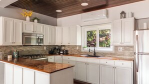 Una cocina moderna con armarios blancos, encimera de madera, electrodomésticos de acero inoxidable y ventana con vistas a zonas verdes.