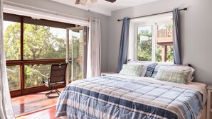 Un dormitorio con una cama grande, un ventilador de techo y vistas al exterior a través de un ventanal corredero.