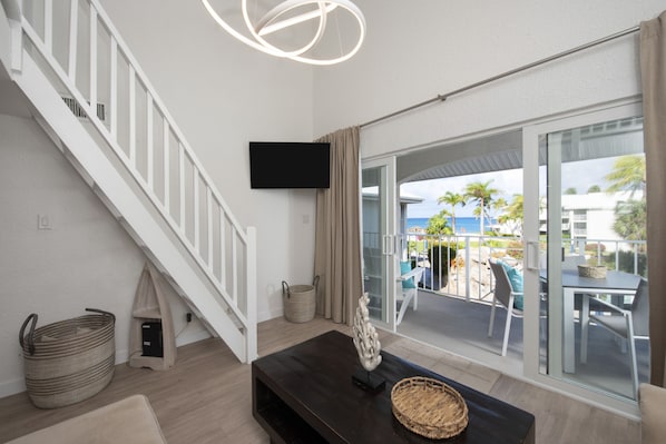 A modern living room with a staircase, a flat-screen TV, and a view of the outdoors.