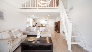 Ein geräumiger Wohnbereich mit hoher Decke, einer Treppe und einer Küche im Hintergrund.