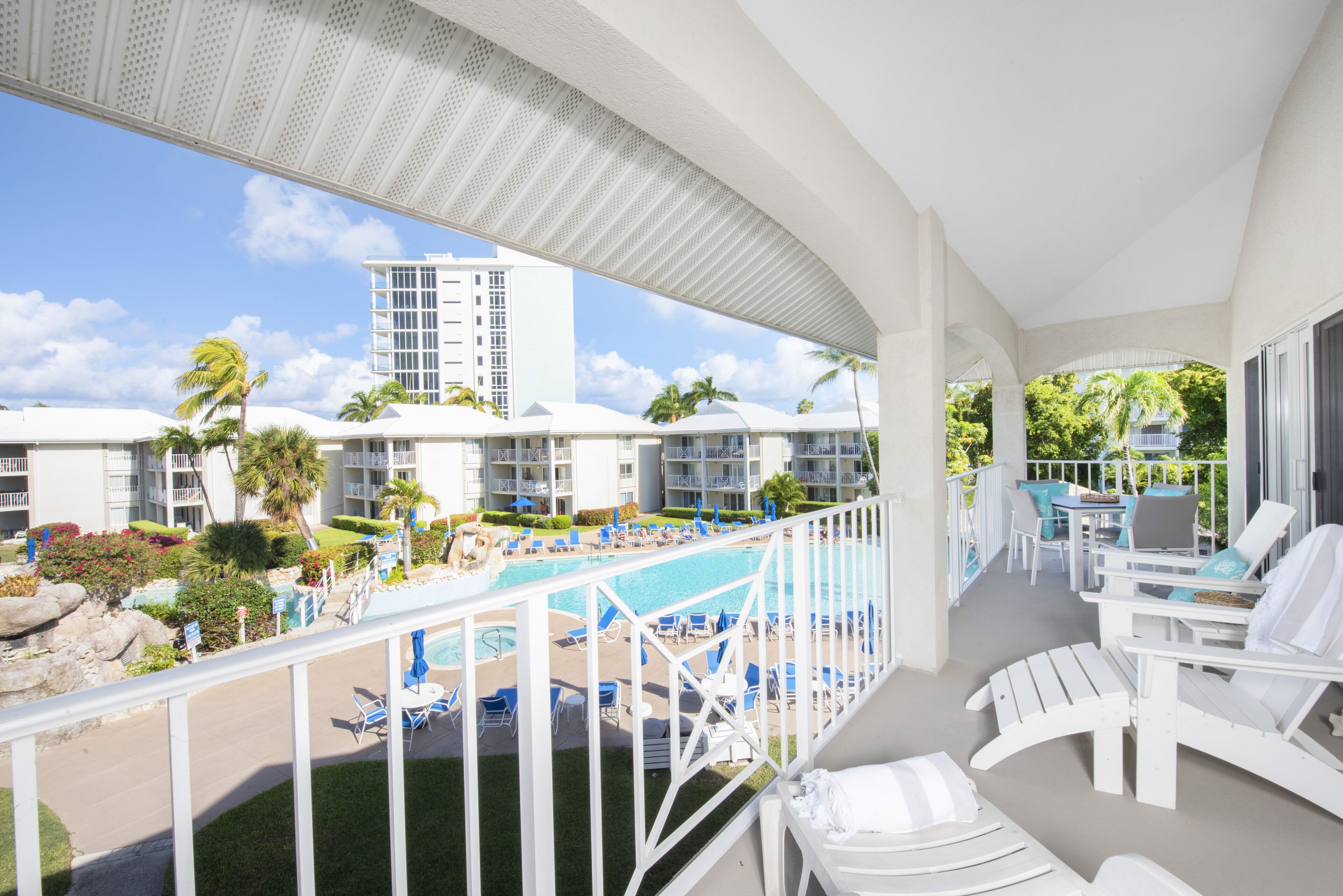 A hotel balcony with a pool, lounge chairs, and a view of the pool area.